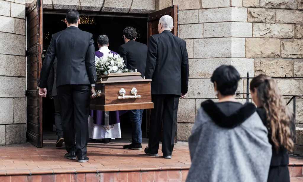 People carrying a casket with white flowers into a church.