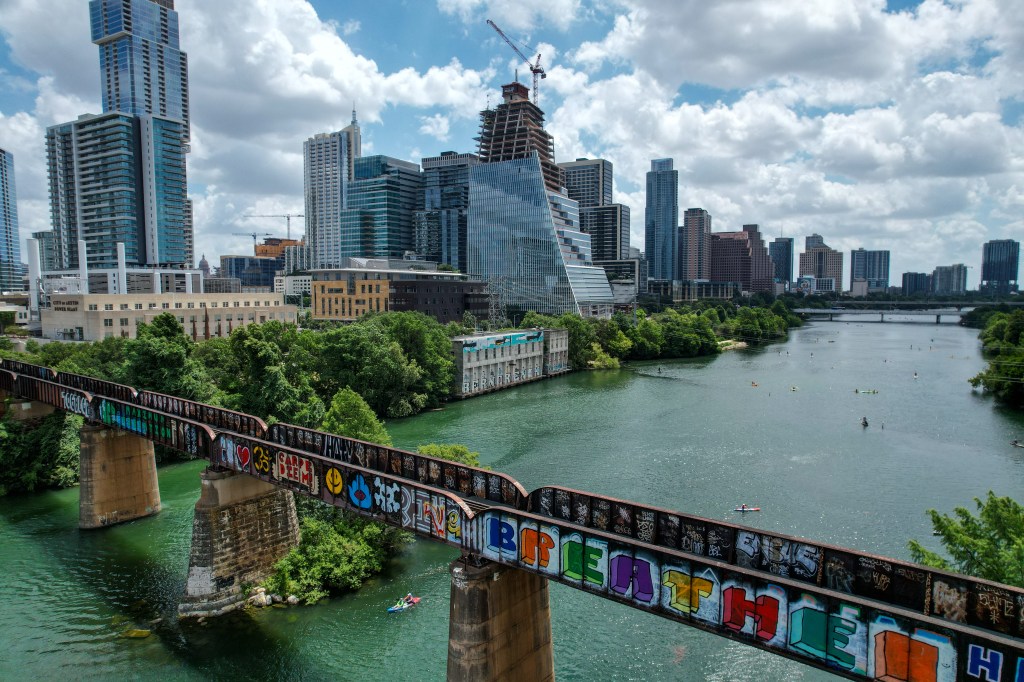Downtown Austin skyline from the west, looking east over Lady Bird Lake and a bridge covered in graffiti.