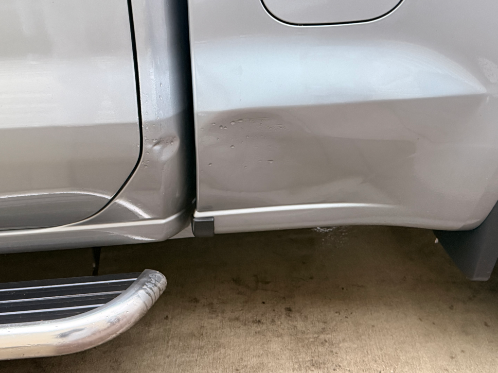 A large dent on the side of a silver truck.