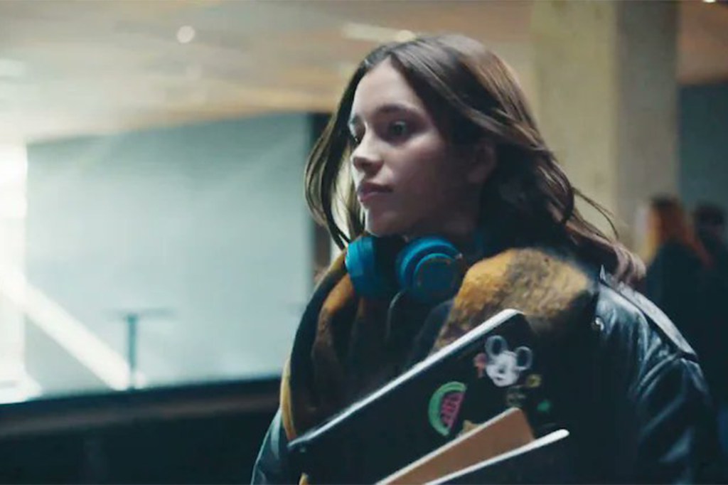 A woman with blue headphones around her neck, holding a laptop with a watermelon sticker on it.