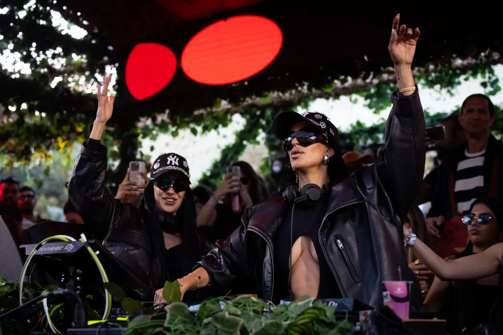 DJs Pitty Bernad and Belah performing on stage, raising their hands in front of DJ equipment.