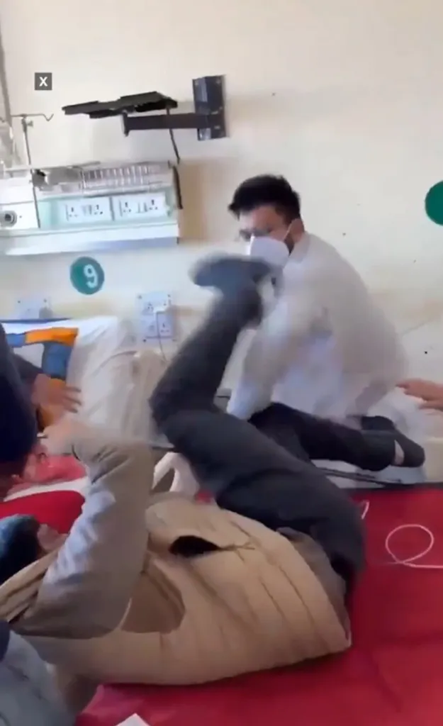 A doctor punching a patient on a bed while others try to intervene.