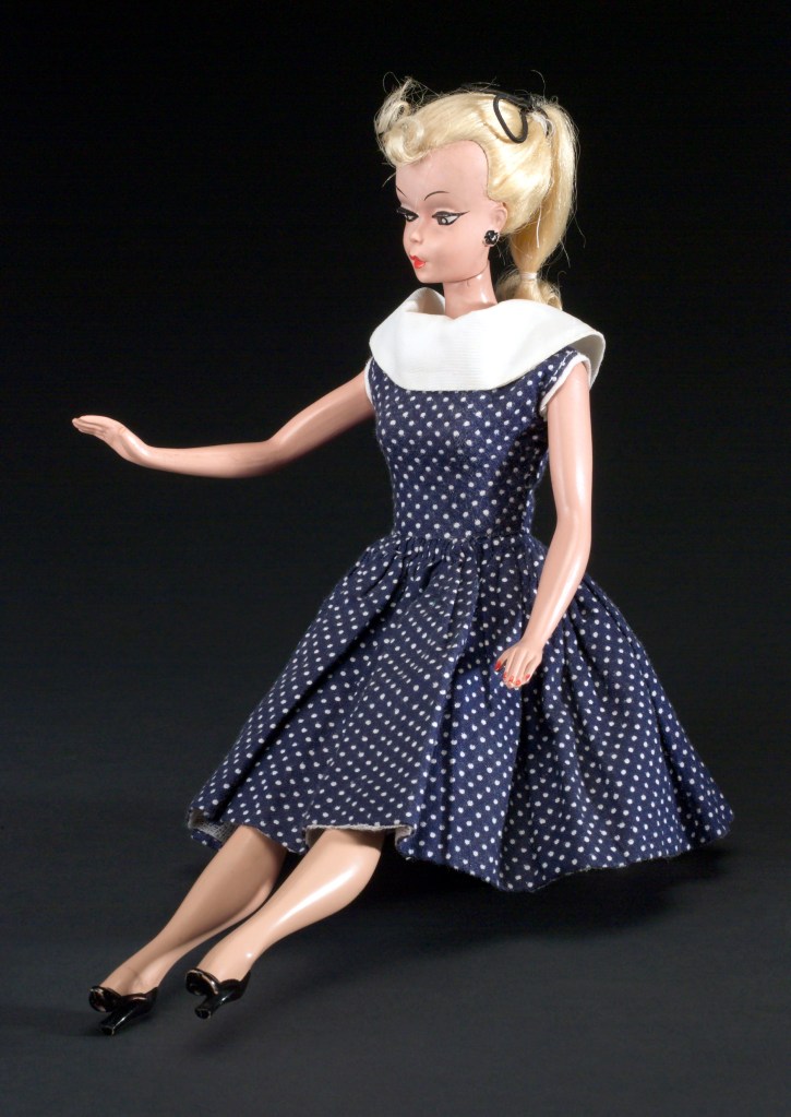 A Bild Lilli doll with blonde hair, wearing a blue polka-dot dress.