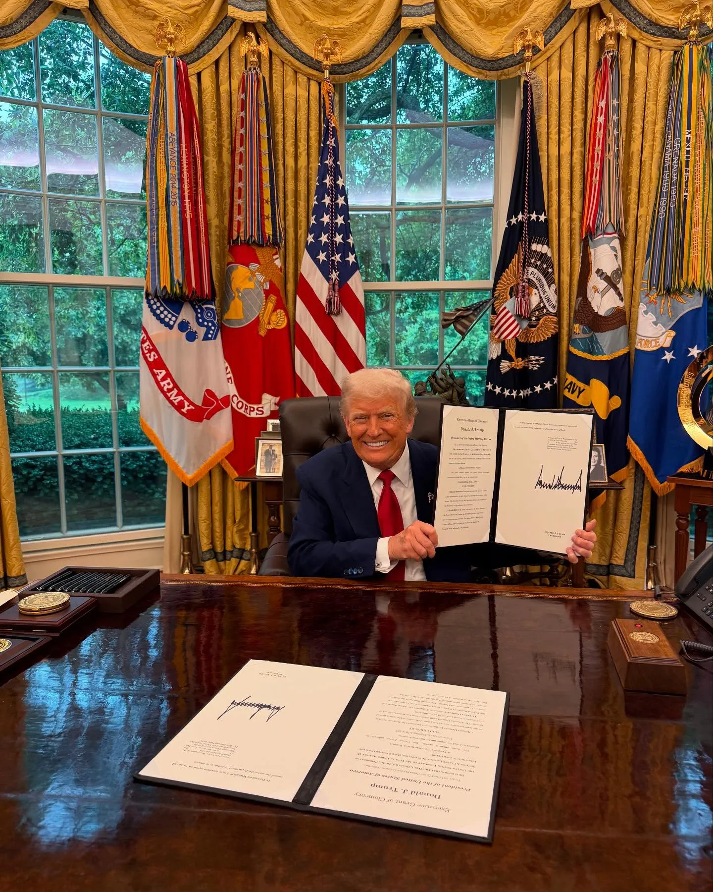 Donald Trump in the Oval Office holding up an 