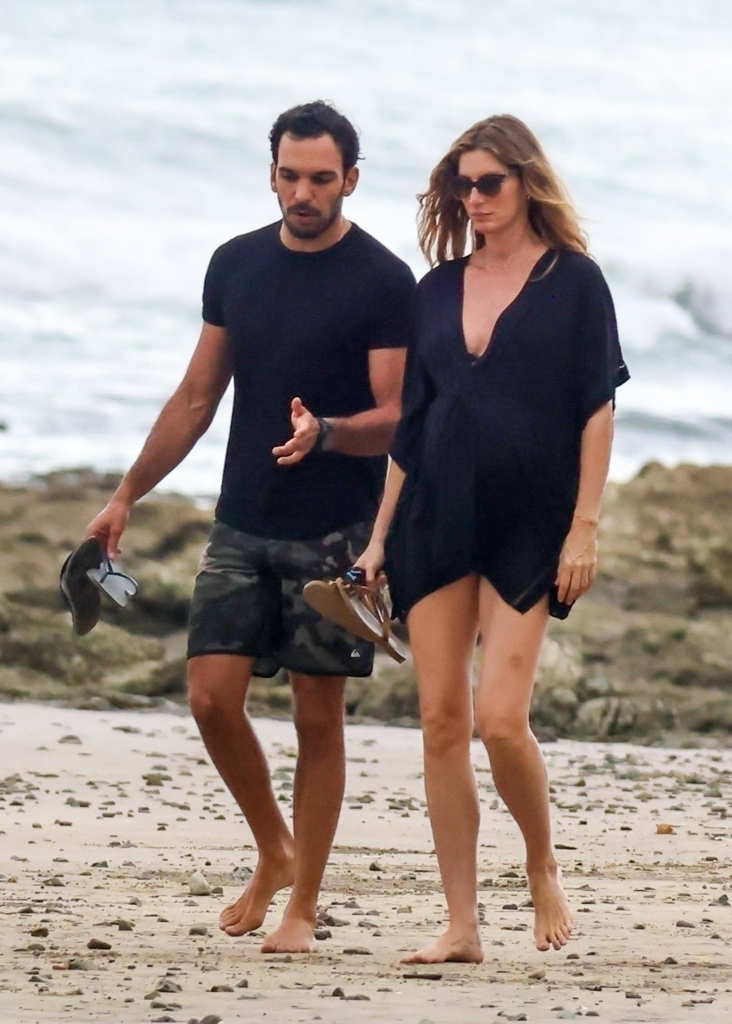 Gisele Bündchen and Joaquim Valente walking barefoot on a rocky beach.