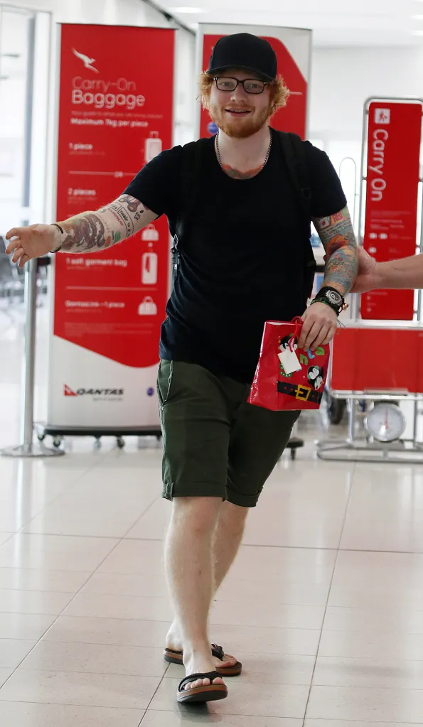 Ed Sheeran departing Perth Airport, holding a red gift bag.