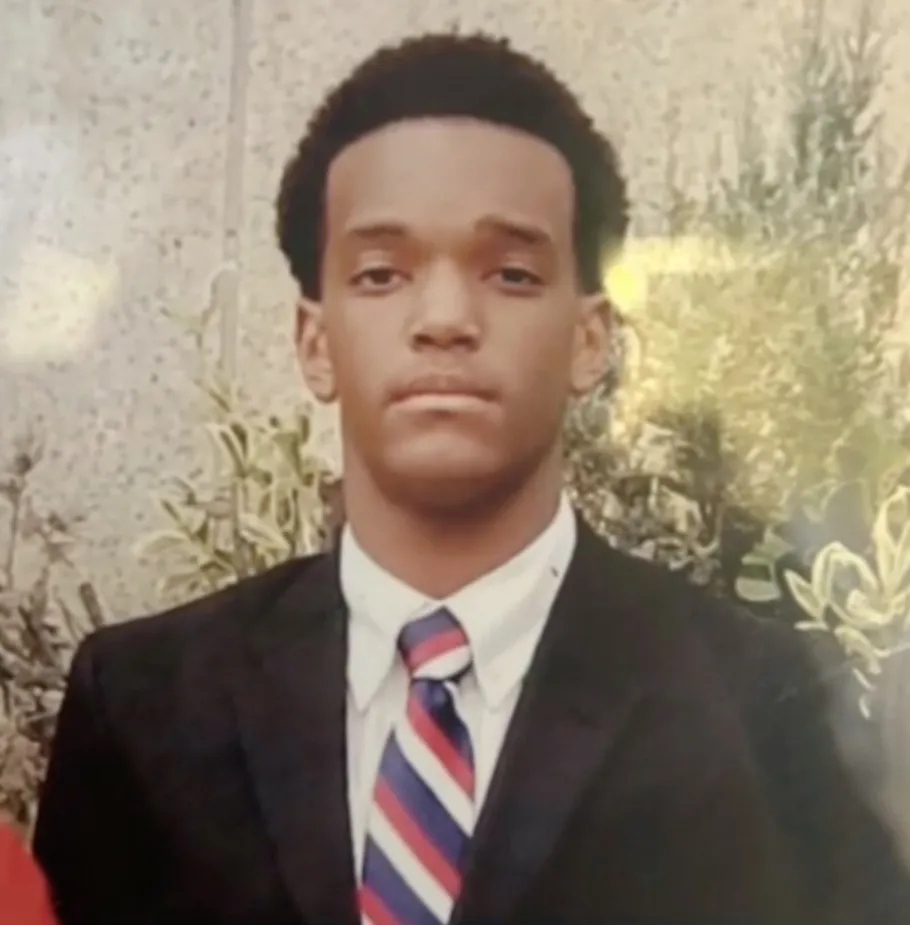 Edeedson Cine Jr. in a black suit, white shirt, and red, white, and blue striped tie.