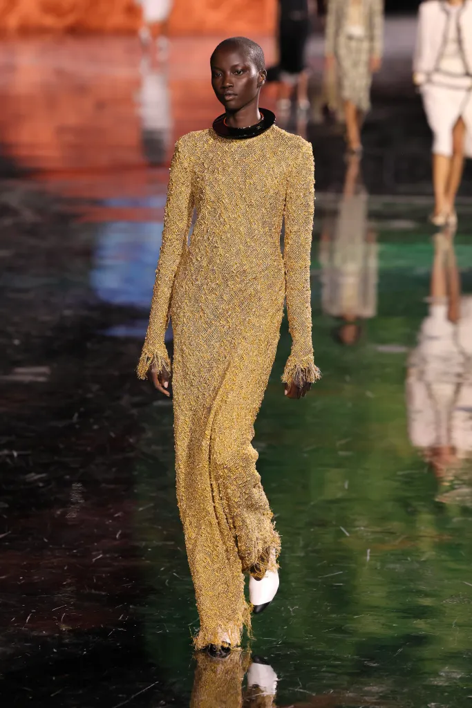 Anok Yai on the Chanel Spring/Summer 2026 runway wearing a gold textured long-sleeve dress with a black and orange choker.