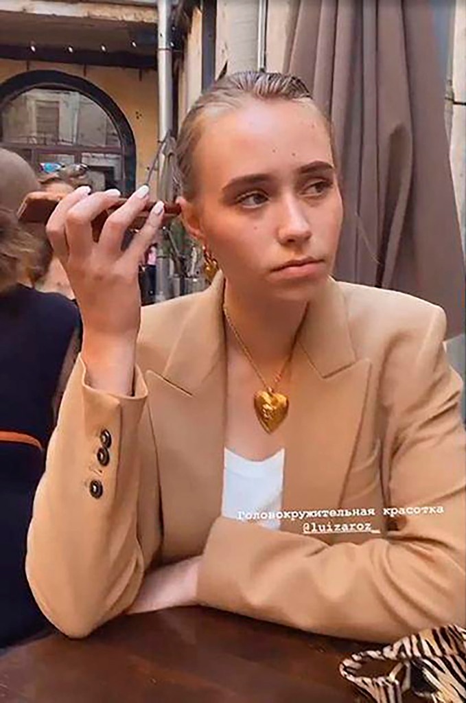 Elizaveta Krivonogikh wearing a brown blazer, a white top, a golden heart-shaped necklace and earrings, and holding a phone to her ear.