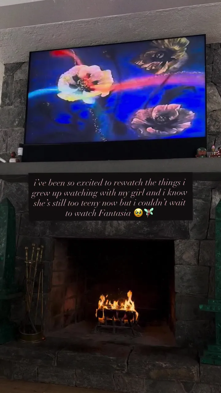 A TV mounted above a lit fireplace, displaying an image from Disney's Fantasia with a caption below it.
