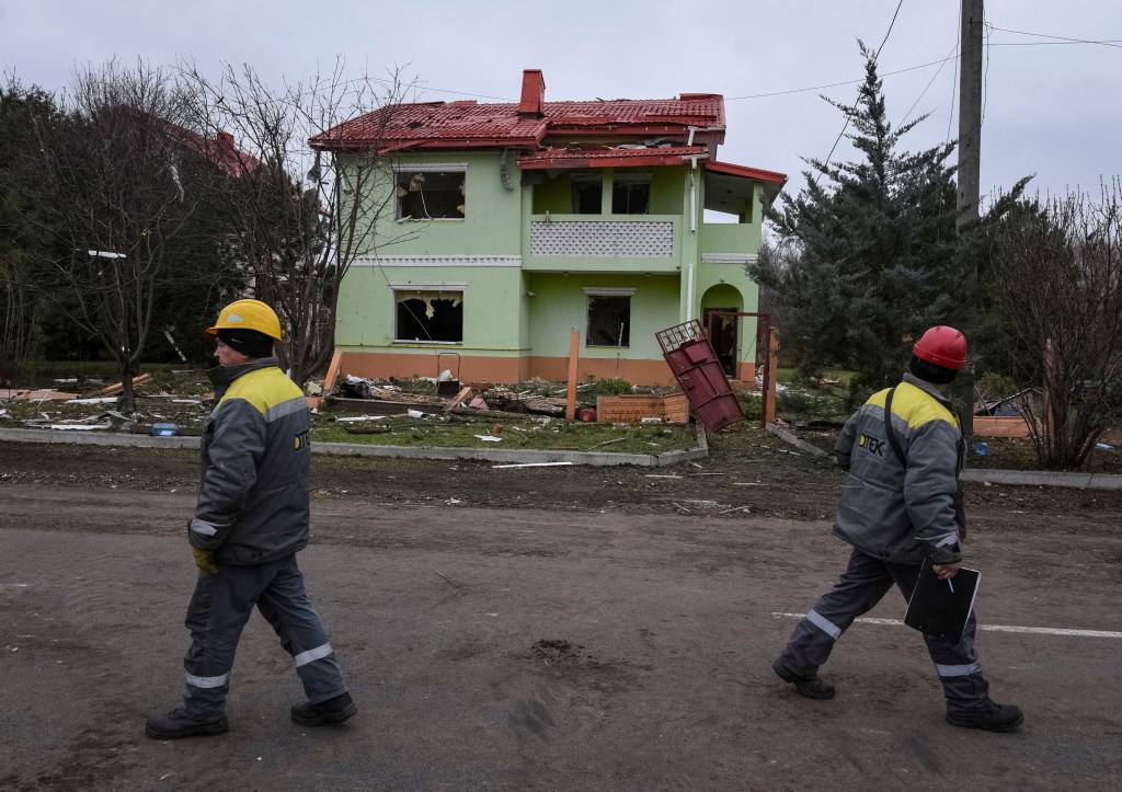 Electric company workers walk near a damaged building after the strike in the Dnipro region of Ukraine.