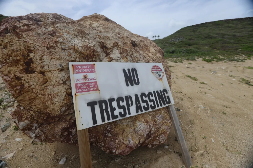 No Trespassing sign by a large rock on a beach.