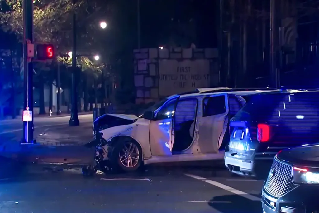 Wrecked white SUV with doors open and a damaged front end on a city street at night, with a church sign in the background.