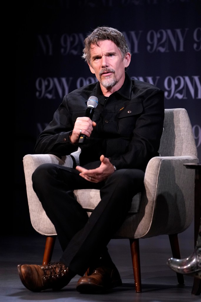 Ethan Hawke holding a microphone and talking while seated in a chair.
