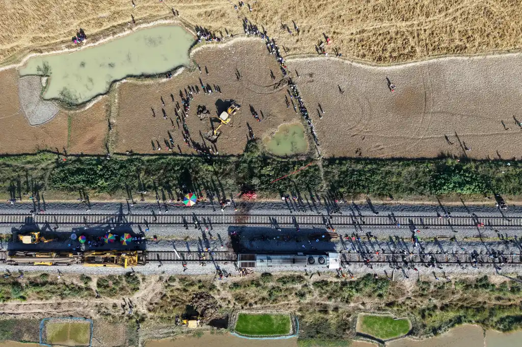 Aerial view of a train next to an excavator digging a pit to bury a wild elephant after it was hit by a train.