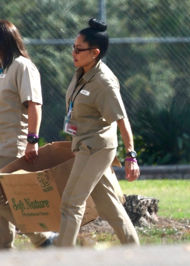 Jen Shah in a tan uniform, glasses, and a bun carrying a cardboard box with another inmate.