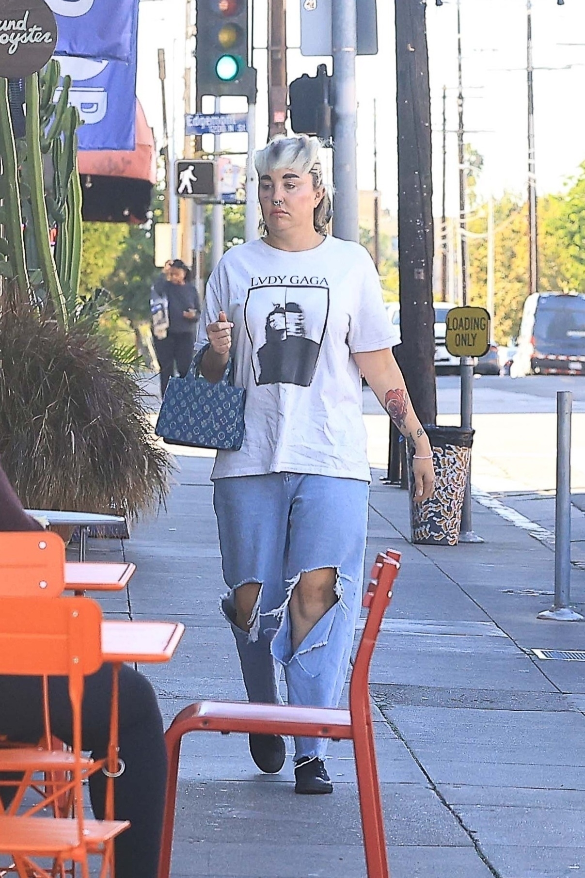 Amanda Bynes walks on a sidewalk wearing a white Lady Gaga t-shirt and ripped jeans.