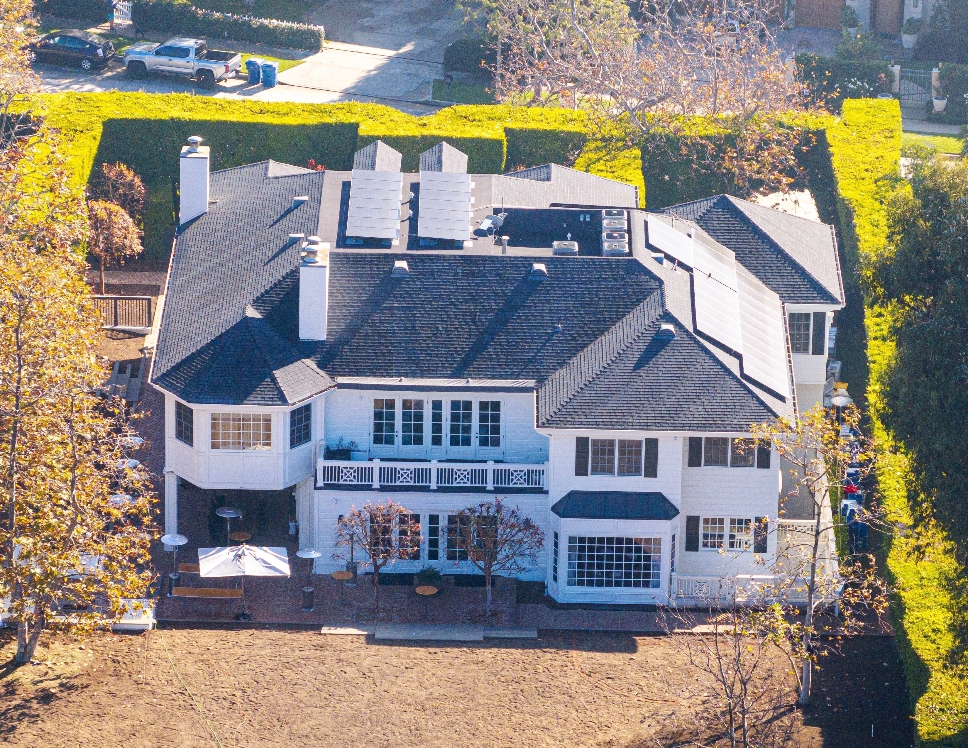 Aerial view of Conan O'Brien's white, two-story Brentwood home with a dark roof and large hedges.