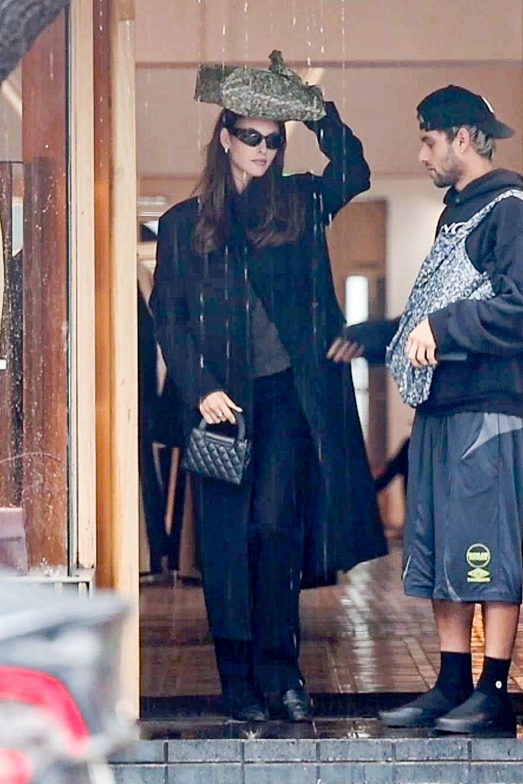 Vittoria Ceretti holding an object over her head to shield from rain, standing with Leonardo DiCaprio.