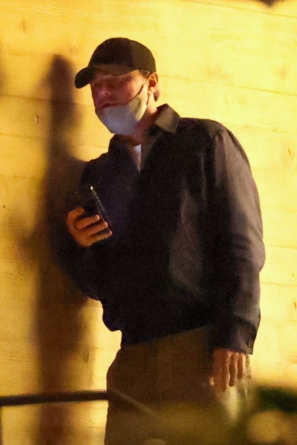 Leonardo DiCaprio wearing a black cap and face mask, holding a phone.