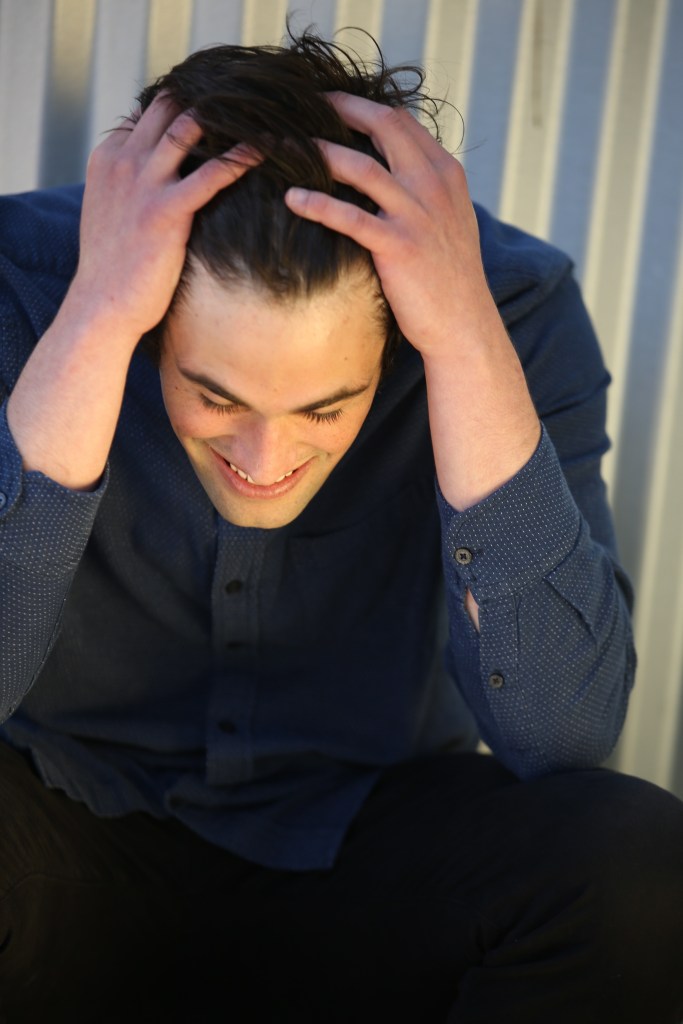 Nick Reiner with his hands in his hair, smiling down.