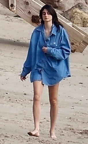 Romy Reiner walking barefoot on Malibu Beach wearing an oversized blue shirt.
