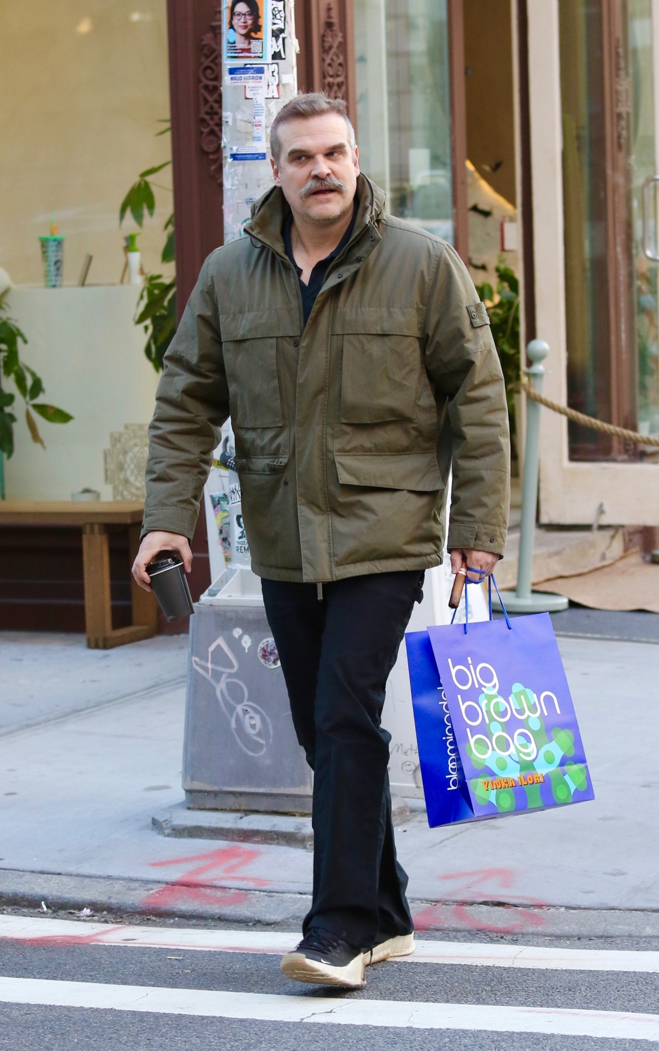 David Harbour walking in New York City with a Bloomingdale's shopping bag and a coffee cup.