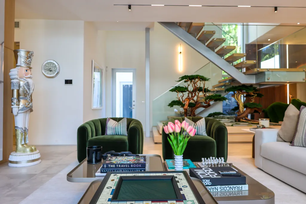 Larsa Pippen's house decorated for Christmas, featuring a large nutcracker statue, green armchairs, a coffee table with books and a game, and a modern staircase.