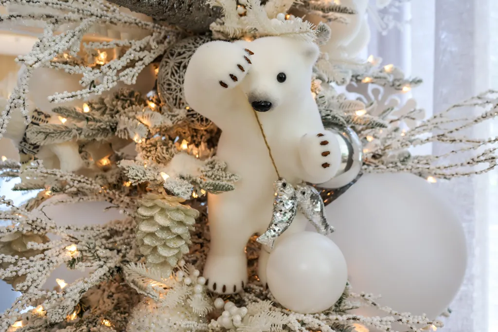A Christmas tree decorated with white and silver ornaments, including a polar bear holding two fish and white baubles.