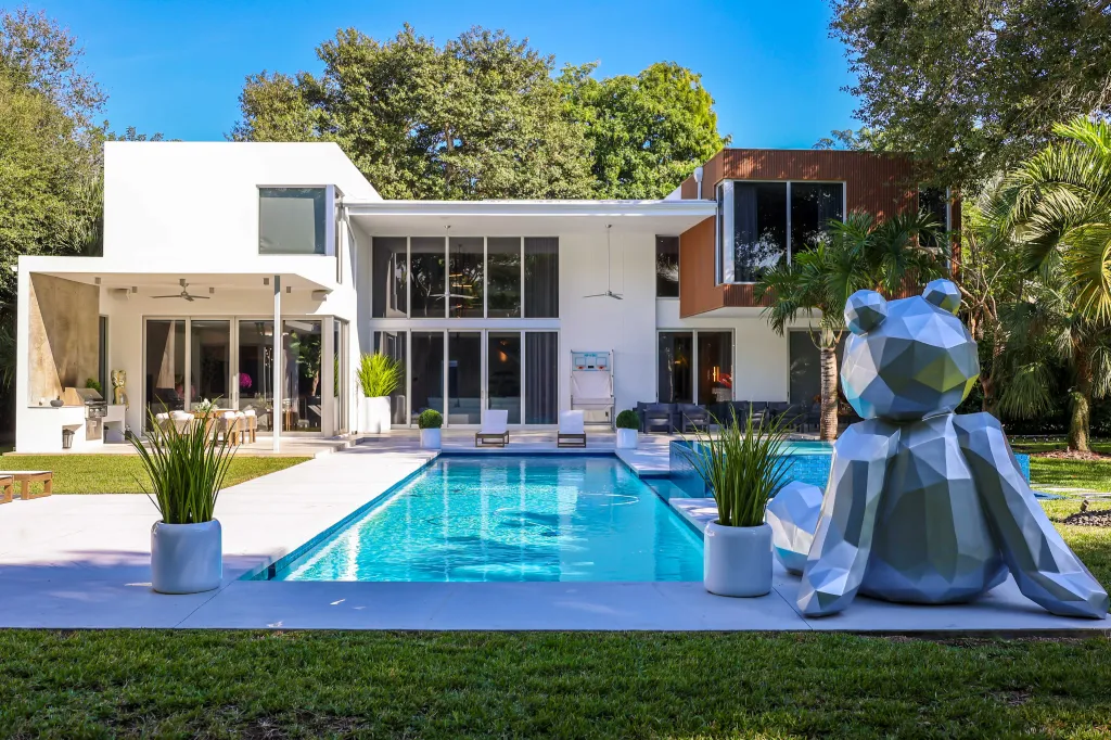 Modern house with pool and large geometric teddy bear statue in front.