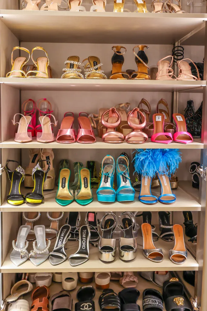 A closet with several shelves full of designer high heels in various colors and styles.