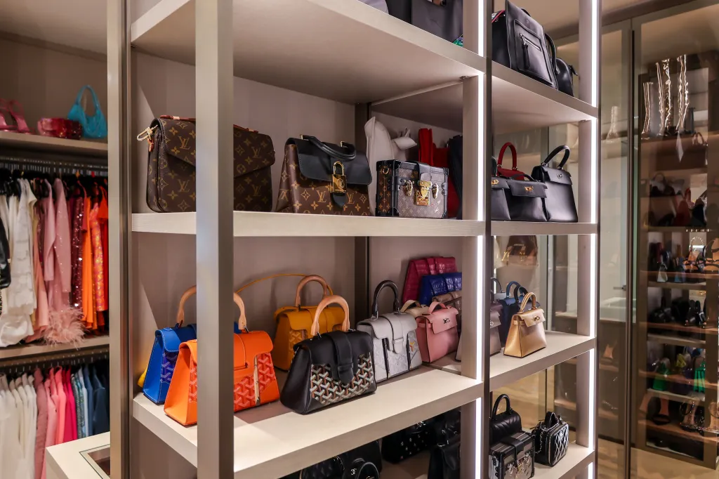 A custom closet with several shelves displaying designer handbags, and racks of clothes.
