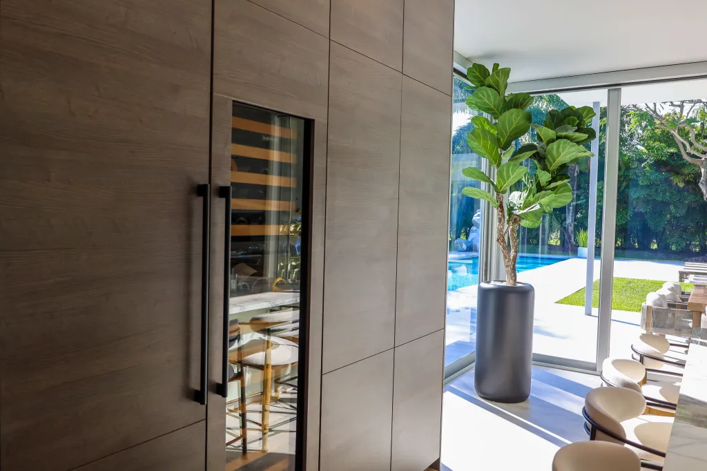 Wine cooler integrated into wooden cabinetry with view of outdoor pool area.