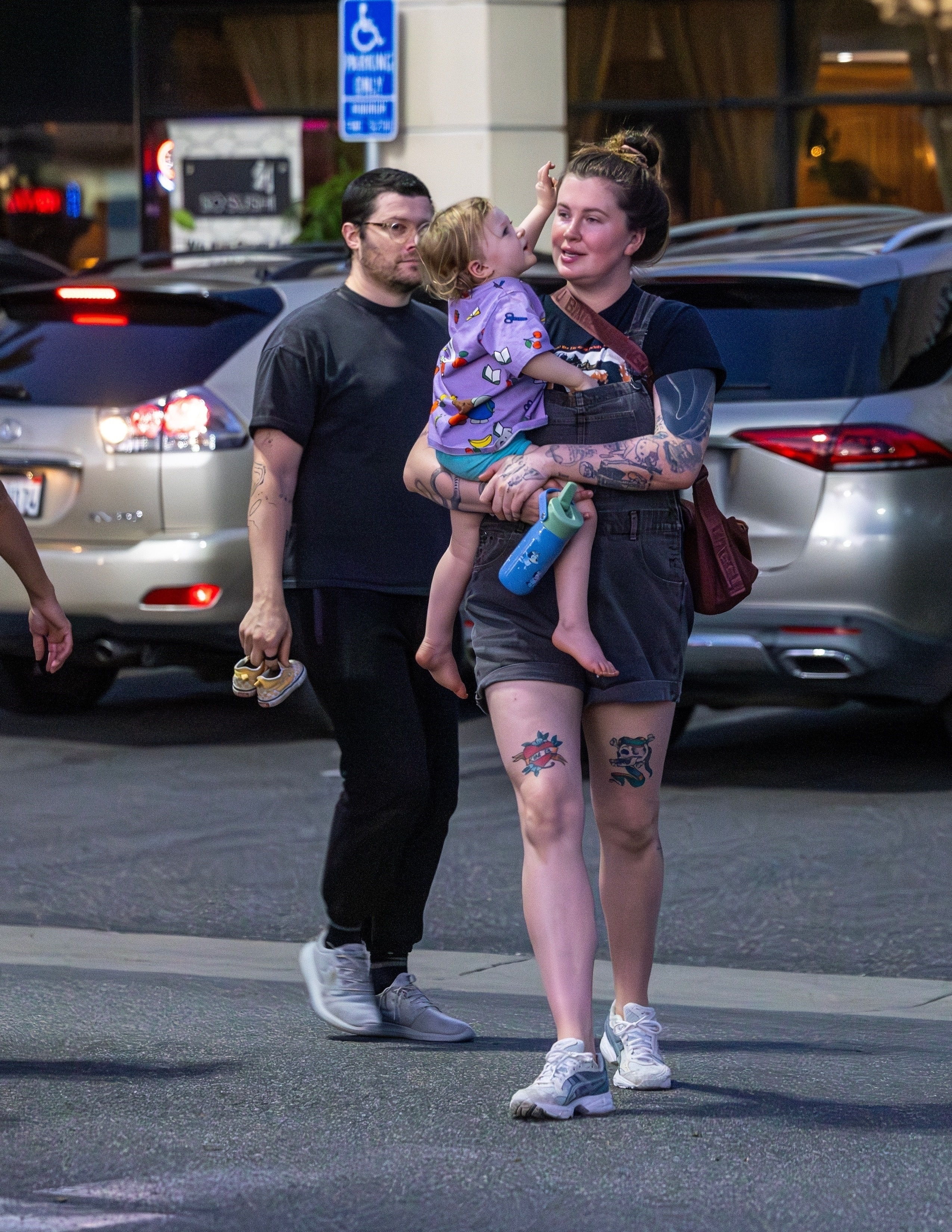 Ireland Baldwin carrying her child while RAC carries their child's small yellow shoes.