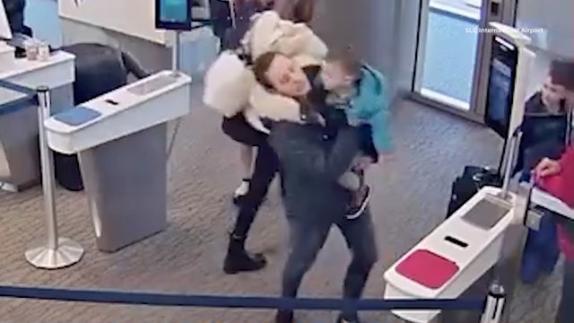 A mother carries one child and another walks with her through a security checkpoint at Salt Lake City International Airport.