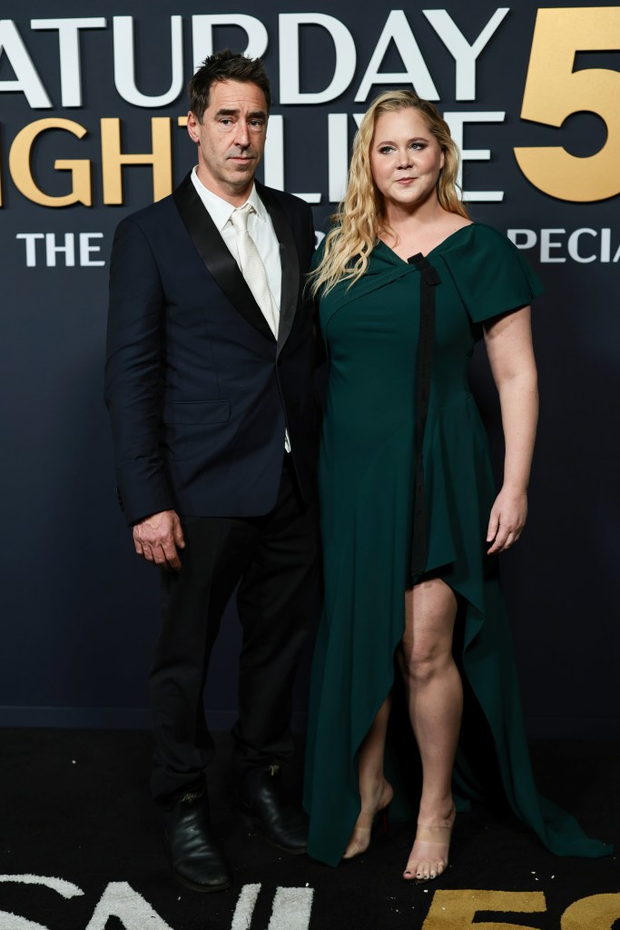 Chris Fischer in a black tuxedo and Amy Schumer in a green dress on the red carpet.