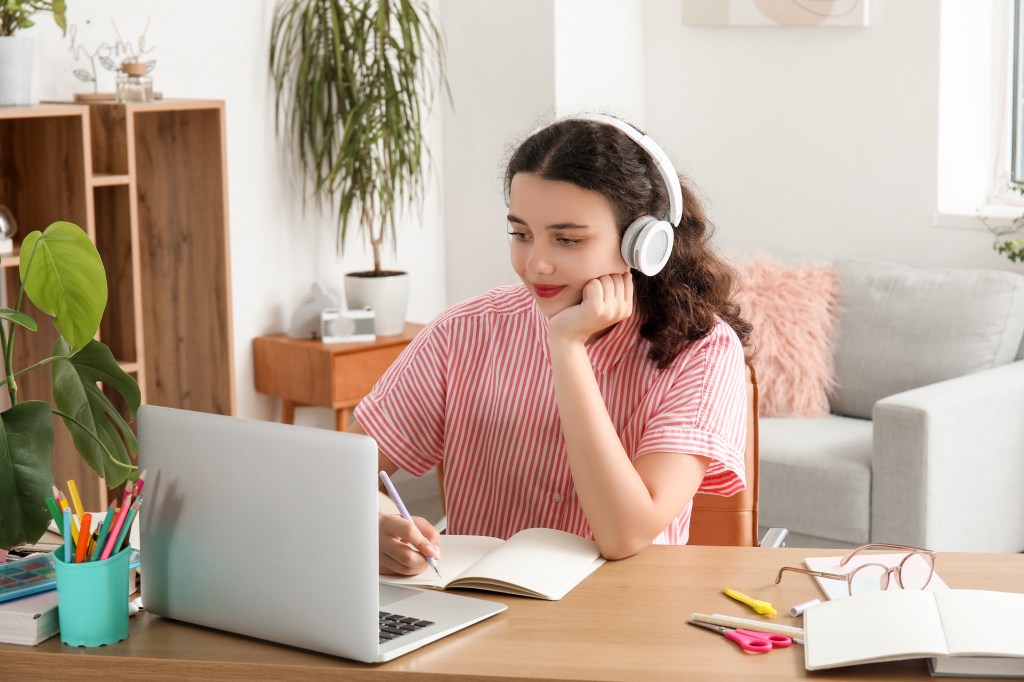 Female student in headphones with a laptop doing lessons at home.