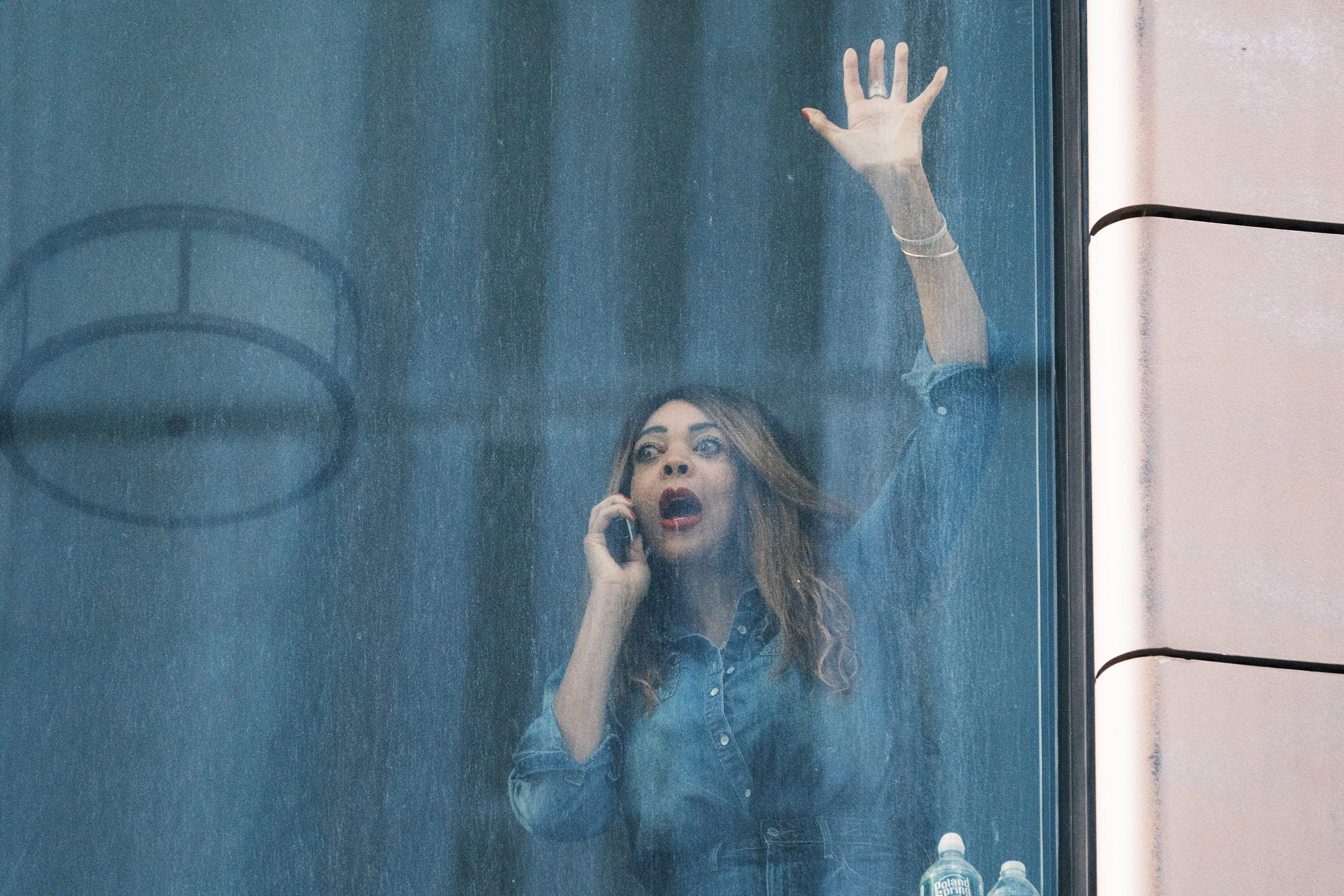 Wendy Williams, holding a phone to her ear and with a shocked expression, waving her hand through a window.
