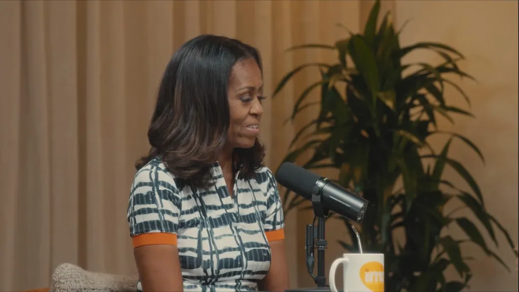Michelle Obama speaking into a microphone during a podcast recording.