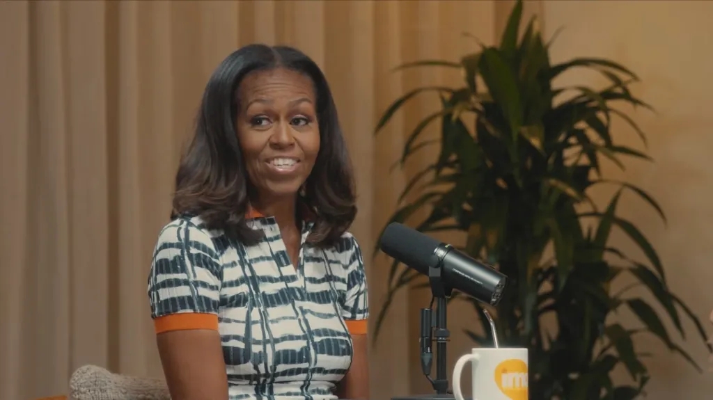 Michelle Obama smiling while sitting next to a microphone and a mug.