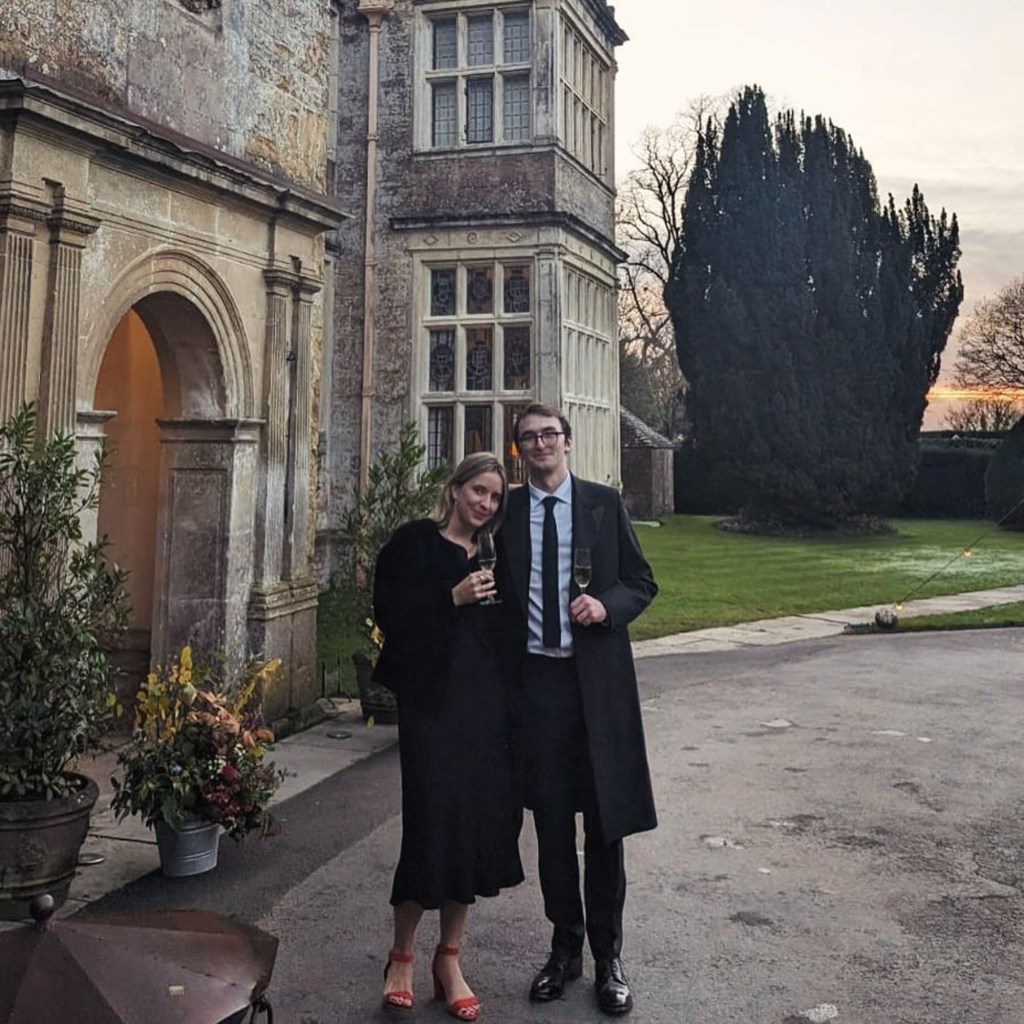 Isaac Hempstead Wright and his wife in front of a stone building, holding champagne glasses.