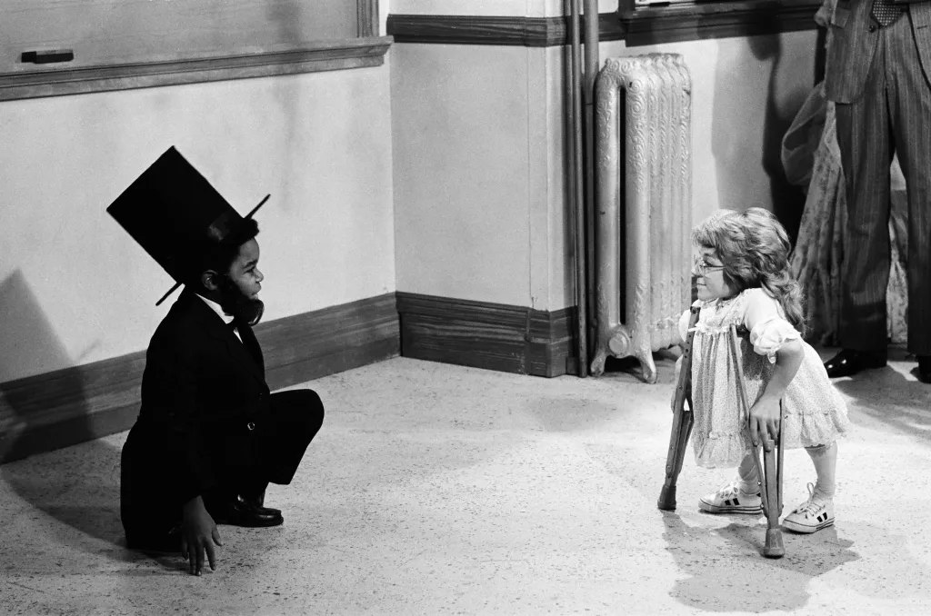 Gary Coleman as Arnold Jackson in an Abraham Lincoln costume crouches facing Melanie Watson as Kathy Gordon on crutches.