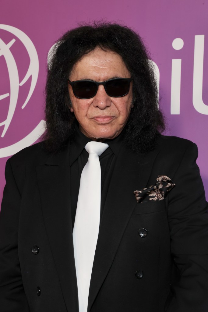 Gene Simmons wearing sunglasses, a black suit, and a white tie.