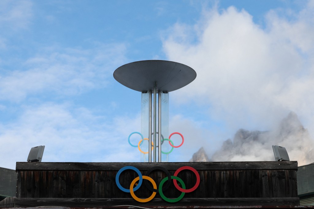 Olympic brazier and rings in front of mountains with white clouds.