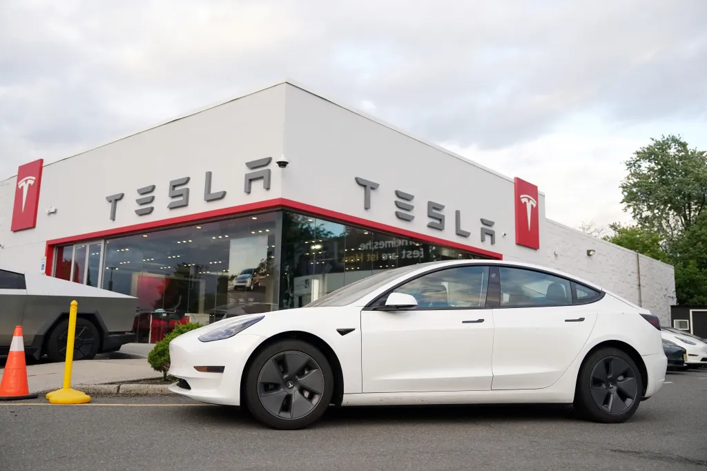 A white Tesla car parked in front of a Tesla dealership in Paramus, New Jersey.