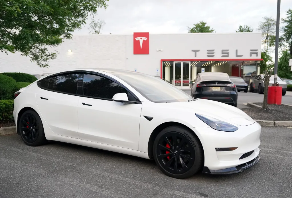 A white Tesla Model 3 car parked in front of a Tesla dealership.