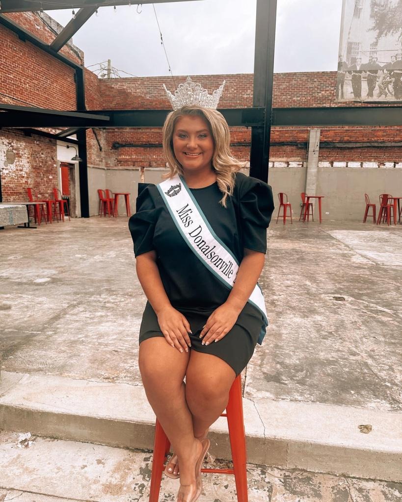 Trinity Poague, Miss Donalsonville, wearing a crown and sash, sitting on a red stool.