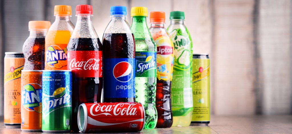 Bottles and cans of assorted global soft drinks including Coca-Cola, Pepsi, Sprite, Fanta, Lipton, Schweppes, and Mirinda.