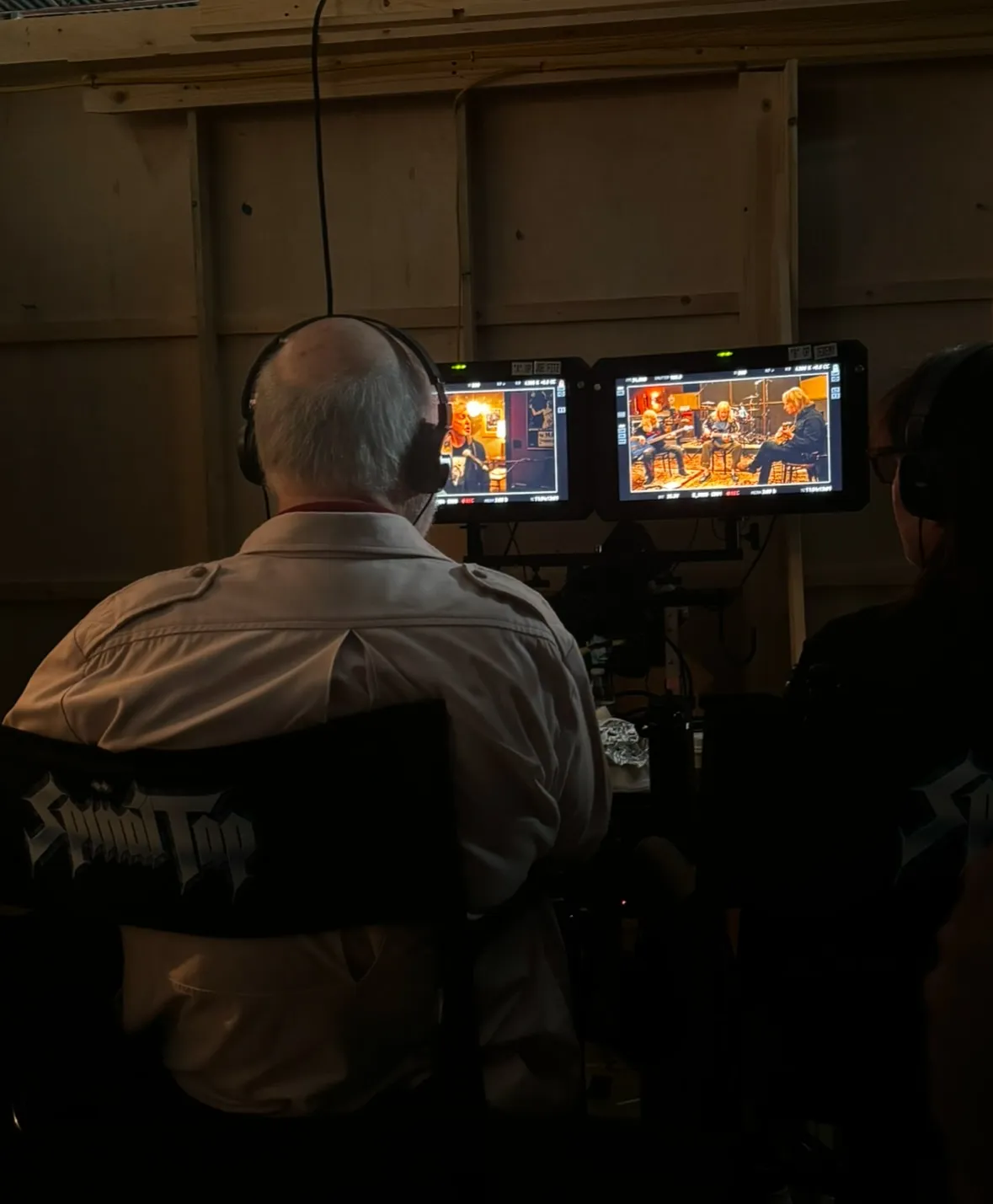 Rob Reiner and another person watching monitors displaying a band, Spinal Tap, playing.