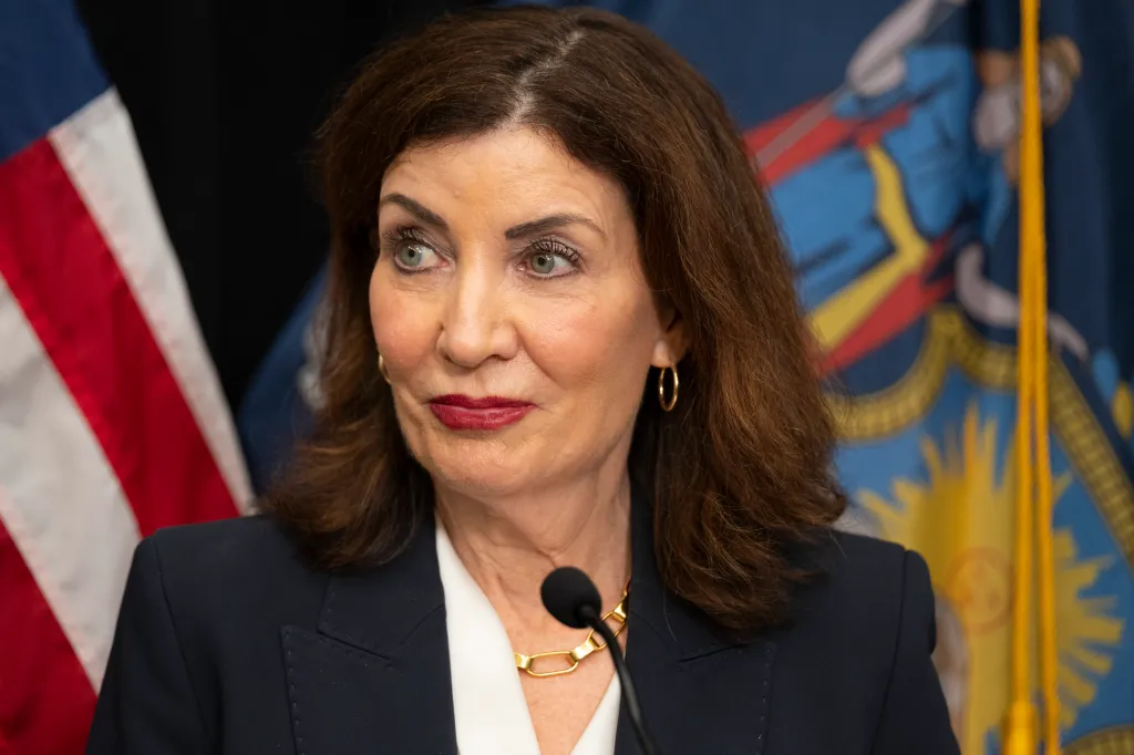 Governor Kathy Hochul speaking at an event, with the US flag and New York State flag in the background.